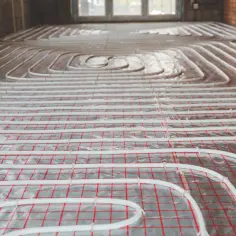 Układanie rurek ogrzewania podłogowego na folii z siatką. Kluczowe jest dobranie odpowiedniej grubości styropianu pod wylewkę, by zapewnić efektywne ogrzewanie.