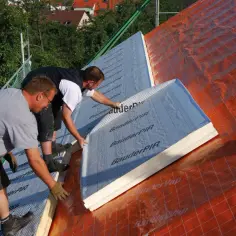Dwóch budowlańców układa płyty termoizolacyjne na dachu. To świetny sposób, czym ocieplić stary dom, zapewniając mu komfort i oszczędność energii.