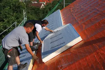 Dwóch budowlańców układa płyty termoizolacyjne na dachu. To świetny sposób, czym ocieplić stary dom, zapewniając mu komfort i oszczędność energii.