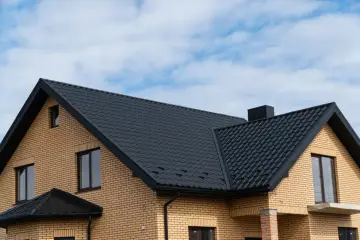 Nowy dom z żółtej cegły z czarnym, falistym dachem. Idealna jaka papa na dach zapewnia ochronę przed deszczem.